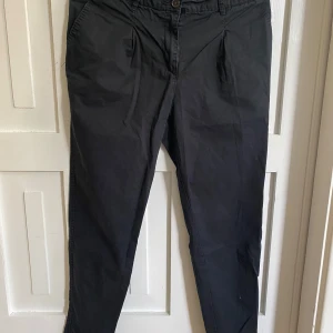 Svarta byxor från H&M - Svarta byxor från H&M med normal passform och klassisk design. Byxorna har knapp och dragkedja framtill samt snedställda fickor. Perfekta för en stilren och enkel look.