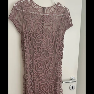 Rosa långklänning med broderade detaljer - Säljer en unik rosa klänning med korta ärmar och vackra broderade mönster över hela tyget. Klänningen har rund halsringning och dragkedja i ryggen. 