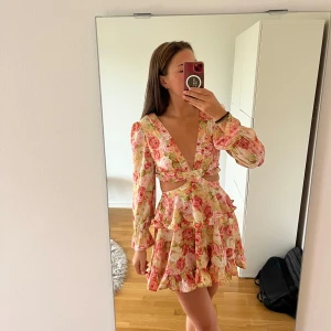 Blommig klänning - Säljer en superfin blommig klänning med volanger och v-ringning. Klänningen har långa ärmar, cut-out detaljer i midjan och omlottkänsla framtill. Färgerna går i rosa, grön och beige med ett romantiskt ros-mönster. Perfekt för sommarens alla tillfällen!