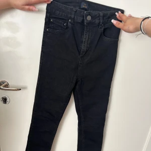Svarta skinny jeans - Säljer ett par svarta skinny jeans med klassisk femficksdesign och hög midja. Jeansen har dragkedja och knapp framtill samt smala ben. Perfekta till vardags och enkla att matcha med olika toppar.
