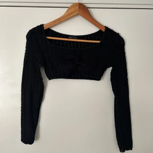 Svart croppad långärmad topp - Säljer en svart croppad topp med lång ärm och rundad urringning. Toppen har en ribbad struktur och är perfekt för att skapa en trendig look. Passar snyggt till både jeans och kjol.