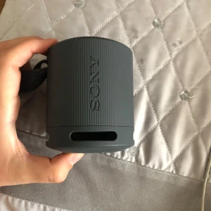 Sony trådlös högtalare  - Bilderna visar en bärbar högtalare från Sony, inte en bok. Produkten är kompakt, har kontrollknappar för volym och uppspelning, samt en USB-C laddningsport. Perfekt för musik på språng.