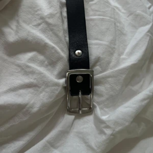 Svart bälte med silverfärgat spänne - Säljer ett klassiskt svart bälte med ett fyrkantigt silverfärgat spänne. Bältet har en enkel och stilren design, perfekt för att lyfta vilken outfit som helst. Varan är i bra skick men precis som det syns på bilden så har lite av den silvriga färgen lossnat.🤍
