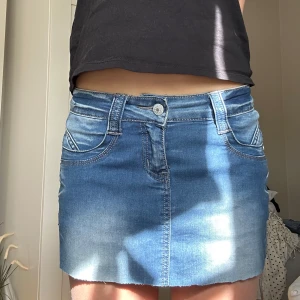Blå jeanskjol med fickor - Säljer en klassisk blå jeanskjol med normal passform och fem fickor. Kjolen har bälteshällor och stängs med knapp och dragkedja framtill. Perfekt att styla med en enkel topp eller hoodie.