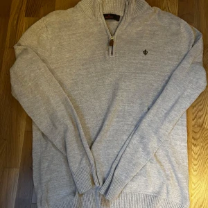 Morris Quarter zip - Säljer en beige stickad tröja från Morris med halv dragkedja och ribbad krage. Tröjan har lång ärm och en liten broderad logga på bröstet, Perfekt för att vara lite uppklädd eller med en skjorta!