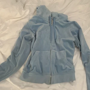 Ljusblå velour hoodie från Juicy Couture - Säljer en ljusblå hoodie i mjuk velour från Juicy Couture. Jackan har dragkedja framtill, huva med snörning och två fickor. Perfekt för en avslappnad och trendig look. En ny kostar 1200