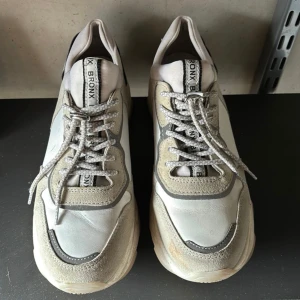 Chunky sneakers Bronx  - Säljer ett par chunky sneakers från Bronx i vitt och beige med silvriga detaljer samt reflexvid de beiga partierna. Köpta på Nelly. De är använda men i bra skick, enligt bilderna. Storlek 39