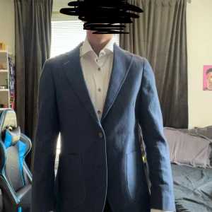 Mörkblå kavaj från Dressmann - Säljer en mörkblå kavaj från Dressmann i slim fit-modell. Kavajen har två knappar framtill, två fickor och ett färgglatt fjärilsmönstrat innerfoder. Perfekt för dig som vill ha en stilren och modern look. Har bara använts i fåtal stunder under högtider.