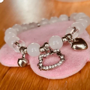 Elastiskt armband med Hello Kitty!  - Elastiskt armband med vita pärlor och berlocker med strass och Hello Kitty-motiv. Nytt!