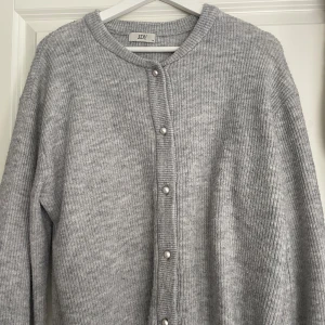 Ljusgrå stickad kofta från JDY - Mysig ljusgrå stickad kofta från JDY med pärlknappar framtill. Koftan har rund halsringning och långa ärmar. Perfekt att slänga på sig när det är kyligt ute.