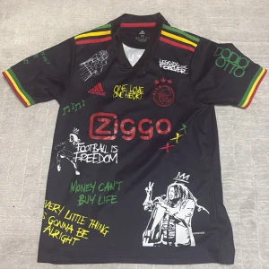 Ajax x Bob Marley edition fotbollströja - Säljer en svart Ajax fotbollströja från Adidas med Ziggo-logga och Bob Marley-tryck. Använd fåtal gånger!