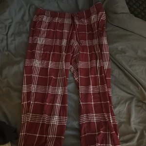 Vinröda rutiga byxor från Kappahl - Säljer ett par vinröda pyjamasbyxor från Kappahl med vitt rutmönster och resår i midjan. Byxorna har en avslappnad passform. Säljer pga för korta🤍