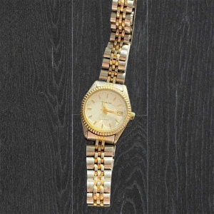 Guld- och silverfärgad armbandsklocka från Quartz - Stilren armbandsklocka från Quartz med tvåfärgat armband i guld och silver. Klockan har rund urtavla, guldfärgade detaljer. Perfekt accessoar för att lyfta din outfit. Fint skick. Vet ej om den funkar, kan vara så att de räcker att byta batteri(4)