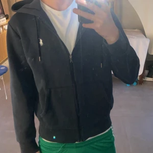 Ralph lauren full zip - Svart hoodie med dragkedja och huva från Polo Ralph Lauren. Klassisk vit logga på bröstet och snörning i huvan. Perfekt för en avslappnad stil.