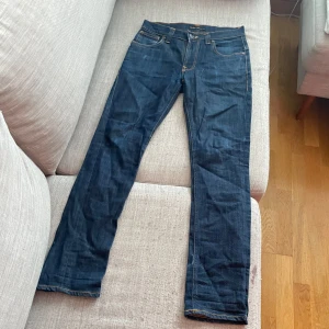 Mörkblå jeans från Nudie Jeans - Säljer ett par mörkblå jeans från Nudie Jeans med klassisk femficksdesign och kontrastsömmar. Jeansen är tillverkade i ekologisk denim och har raka ben. Perfekta för dig som gillar stilrena och tidlösa jeans.