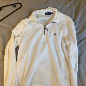 Vit långärmad tröja från Polo Ralph Lauren - Säljer en stilren vit långärmad tröja från Polo Ralph Lauren med halv dragkedja och klassisk broderad logga på bröstet. Perfekt för en clean och sportig look. Tröjan har krage och är riktigt skön att bära.