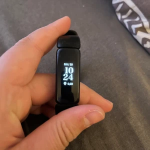 Svart aktivitetsarmband från Fitbit - Säljer ett svart aktivitetsarmband från Fitbit med smal rektangulär display och silikonarmband. Klockan visar tid, datum och steg direkt på skärmen. Perfekt för dig som vill hålla koll på din aktivitet och hälsa.