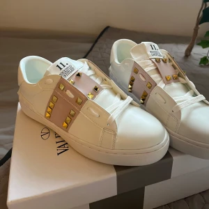 Valentino Garavani Rockstud sneakers i vitt - Säljer ett par vita Valentino Garavani Rockstud sneakers med ljusrosa band och guldiga nitar på. Storlek 40.💕 