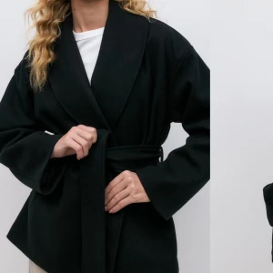 Svart kappa  - Snygg svart gina kappa med bälte i midjan och bred krage. Jackan har lång ärm och en avslappnad passform som ger en modern look. Perfekt att slänga över en hoodie eller t-shirt. Kom privat för mer bilder och våga skicka prisförslag! Nypris är 700kr mitt pris 500kr
