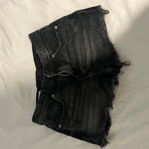 Svarta jeansshorts med fransar från Zara - Svarta jeansshorts från Zara med råa fransade kanter och klassisk femficksdesign. Shortsen har hög midja och en snygg, lite tvättad look. Perfekta för sommardagar när du vill ha en cool och avslappnad stil.