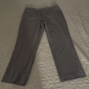 Svarta kostymbyxor från Farah - Snygga svarta kostymbyxor från Farah med klassisk rak passform. Byxorna har bälteshällor, diskreta fickor och är tillverkade i ett mjukt material som känns bekvämt mot huden. Perfekta för en stilren look.