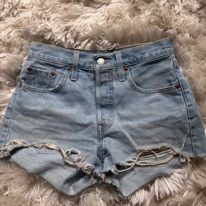 Levi's 501 jeansshorts - Klassiska ljusblå jeansshorts från Levi's modell 501 med råa fransade kanter. Medelhög midja och knappgylf. Perfekta för sommaren och har en avslappnad vintagekänsla. Storlek xs/s.