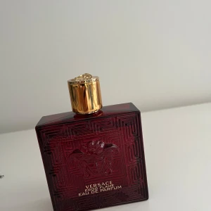 Versace Eros Flame Eau de Parfum 100ml - Säljer en elegant Versace Eros Flame Eau de Parfum i en djup röd flaska med guldlock. Flaskan har ett stilrent mönster och rymmer 100 ml av denna exklusiva doft. Perfekt för den som vill ha en lyxig och intensiv parfymupplevelse. Stark men samtidigt fräsch och med bra prestation. Den bästa Eros! Saknar någon enstaka ml!