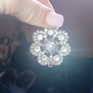 Silverfärgat blomformat hänge med pärla och strass - Säljer ett vackert blomformat hänge i silverfärg med glittrande strass och en pärla i mitten. Perfekt som smyckesdel till halsband eller armband. Ger en elegant och glittrig look. 