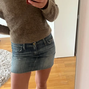 Jeanskjol lågmidjad - Säljer en klassisk blå lågmidjad jeanskjol från med femficksmodell och slitna detaljer. Kjolen är kort och har en snygg tvättad look med knapp och dragkedja framtill. Perfekt för dig som gillar en tidlös denimstil.