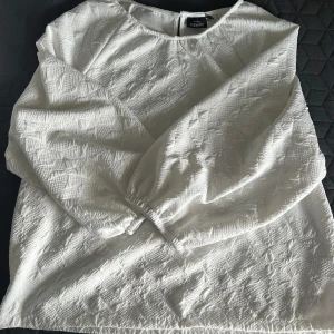 Vit strukturerad trekvartsblus från Kappahl - Säljer en vit blus från Kappahl med strukturerat mönster och rund halsringning. Blusen har puffiga trekvarts ärmar  med resår vid ärmslut och en liten öppning bak i nacken. Perfekt för en stilren look. Skulle säga att den även sitter bra på en M.💞