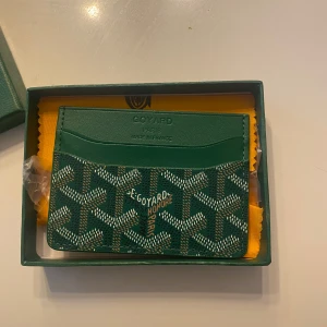 Görn plånbok - Snygg grön plånbok med klassiskt grafiskt mönster i vitt och brunt. Plånboken har flera kortfack och är tillverkad i exklusivt skinn. Kommer i originalask. Perfekt för dig som gillar lyxiga accessoarer.