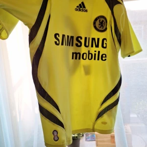 Chelsea bortatröja Terry 26 Adidas riktig lovar lägg gärna prisförslag - Chelsea FC bortatröja i gult med svarta detaljer, Adidas-logga och klubbmärke på bröstet. Tryck med 'Samsung Mobile' på framsidan och 'Terry 26' på ryggen. Kortärmad modell i lätt och ventilerande material, perfekt för fotboll eller samling. Är värd 1400 som ny lägg gärna prisförslag