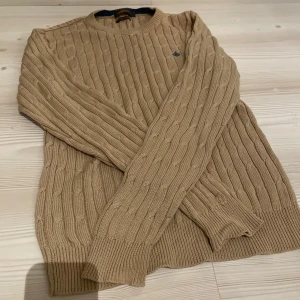 Beige kabelstickad tröja Morris - Kabelstickad beige tröja från Morris i bomull. Klassisk rund halsringning, och diskret blå logga broderad på bröstet. Perfekt för dig som gillar stilren och tidlös look. Storlek Medium. Nyskick! Inga märken, skador eller defekter. Frågor eller funderingar? Bara att höra av sig! 