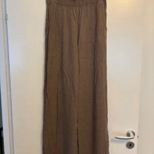 Bruna vida linnebyxor från H&M - Säljer ett par bruna linnebyxor från H&M i storlek S. Byxorna har hög midja med resår, vida ben och två stora fickor bak. Byxorna har även en kort slits på båda sidorna av benen. Perfekta för en chill och avslappnad stil, superlätta och sköna i materialet.