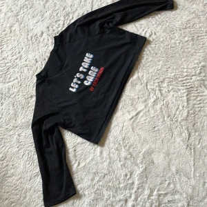 Svart croppad långärmad tröja - Svart croppad långärmad tröja med trycket 'LET'S TAKE CARE OF EACH OTHER!' i vitt, blått och rött framtill. Tröjan har en rund halsringning och är i mjukt bomullsmaterial. Perfekt för dig som gillar statement-plagg med chill vibe. Varken märke eller storlek står på tröjan men skulle säga att den passar en xs eller s