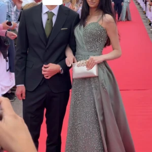 Grön långklänning med pärldetaljer - Säljer en magisk grön långklänning med smala axelband och v-ringning. Klänningen har glittriga pärldetaljer på livet och framtill, samt en vid kjol i satinliknande material. Perfekt för bal eller student! Snygg omlott-effekt upptill och markerad midja. Storleken på klänningen är S men jag har sytt in den till XS. Om det är så att din storlek är S kommer den passa dig utmärkt! 