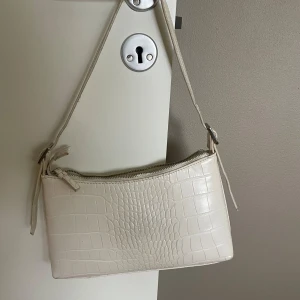 Vit axelväska från NA-KD - Säljer en stilren vit axelväska från NA-KD. Väskan har en smal axelrem och stängs med dragkedja. Perfekt storlek för det viktigaste och ger en clean vibe till din outfit.