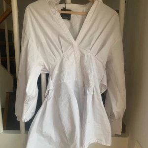 Vit omlottklänning från Gina Tricot - Snygg vit skjortklänning  från bershka  med omlott-design och v-ringning. Klänningen har långa ärmar med knappar vid ärmslut och öppen rygg 