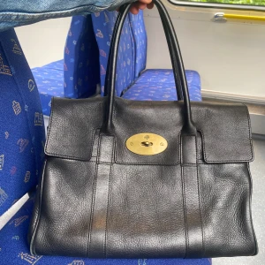 Svart Mulberry Bayswater handväska - Klassisk svart Bayswater handväska från Mulberry i äkta skinn med guldiga metalldetaljer och lås. Väskan har dubbla handtag, innerfack med dragkedja och nyckel i läderfodral. Perfekt storlek för allt du behöver ha med dig. 🤩Väskan är äkta och om du är intresserad kan jag skicka flera bilder😊Postas endast.