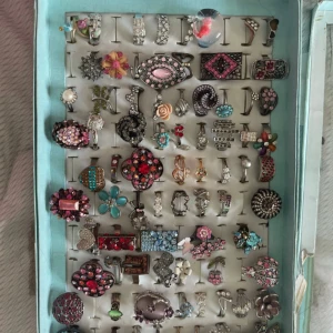 Färgglada statementringar i mixad stil - Samling med unika och färgglada statementringar i olika former och mönster. Ringarna har detaljer som blommor, hjärtan, pärlor och gnistrande stenar i rosa, rött, blått, silver och svart. Perfekt för dig som vill sticka ut med accessoarer och mixa olika stilar. 30kr/styck