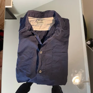  kortärmad skjorta Acne Studios - Kortärmad skjorta från Acne Studios i mörkblå bomull. Klassisk krage, bröstficka och knäppning framtill. Perfekt för en clean och stilren look, funkar lika bra till jeans som till chinos.