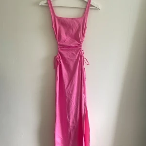Klänning Chiquelle - Rosa långklänning från Chiquelle med slits på ena sidan. Klänningen har en öppning på sidorna som kan justeras. Fint skick, använd fåtal gånger.