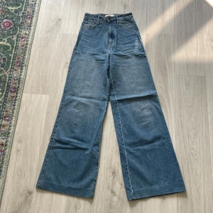 Blå wide jeans från STR, hög midja - Snygga blå jeans från STR med hög midja och riktigt breda ben. Klassisk femficksmodell i jeansmaterial med knapp och dragkedja framtill. Perfekta för dig som gillar en loose och trendig siluett.