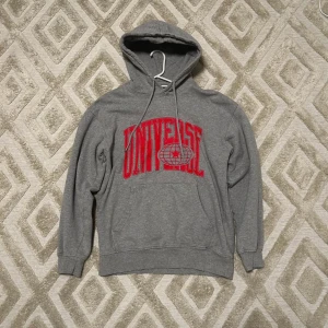 Grå hoodie från Vailent med röd print - Grå hoodie från Vailent med stor röd 'UNIVERSE' print och glob-motiv på bröstet. Klassisk känguruficka, snörning i huvan och ribbade muddar. Perfekt för chill dagar och streetstyle. Mjuk bomullsblandning och relaxed fit.