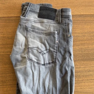 Replay Anbass grå jeans, stl 29 - Snygga Replay Anbass jeans. Jeansen har raka ben och normal passform, tillverkade i mjukt denimtyg. Perfekta för dig som gillar en stilren och avslappnad look. Jeansen sitter bra för en kille mellan 180-170.