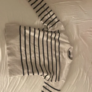 Vit och svart randig stickad tröja - Vit stickad tröja från lager 157 med svart horisontella ränder. Tröjan har rund halsringning, breda ribbade muddar och långa ärmar. Perfekt för dig som gillar en klassisk och chill stil.