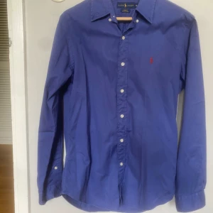 Blå skjorta från Ralph Lauren slim fit - Snygg blå skjorta från Ralph Lauren i slim fit-modell. Perfekt för dig som gillar stilrena plagg med premiumkänsla. Storlek M och mycket bra skick. Hör av er vid intresse!!
