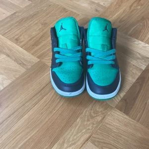 Nike Air Jordan 1 Low svart/grön - Snygga Nike Air Jordan 1 Low sneakers i svart och grön med klassisk Jumpman-logga på plösen och Air Jordan-vinge på hälen. Skorna har snörning, vit sula och är tillverkade i skinn och syntet. Perfekta för dig som vill sticka ut med en färgstark look. Kan gå ner med priset.