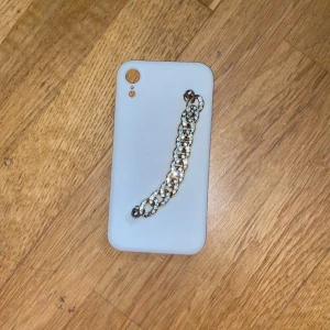 Vit mobilväska med kedjedetalj - Säljer en stilren vit mobilväska med en chunky guldfärgad kedja dekorerad med glittrande stenar. Väskan har ett minimalistiskt utseende och kedjan ger en lyxig touch. Perfekt accessoar för att lyfta din outfit.