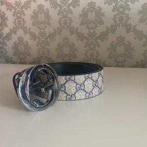 Gucci GG  bälte med silverdetalj - Gucci GG Supreme bälte i beige och blått med klassiskt GG-mönster och stor rund silverspänne med logga. Bältet är gjort i skinn och canvas, och levereras med originalförpackning och dustbag.